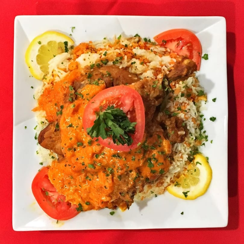 Indian chicken curry with rice, garnished with lemon slices, tomato, and parsley on a white plate.