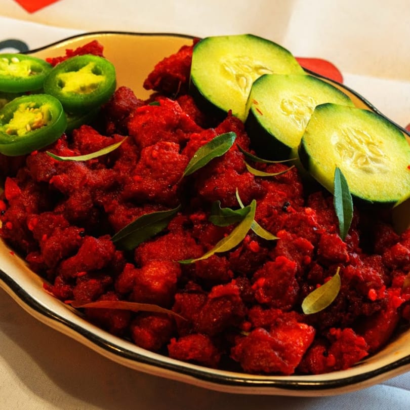 Bright red Indian chicken dish, garnished with green jalapeño slices, cucumber, and curry leaves.