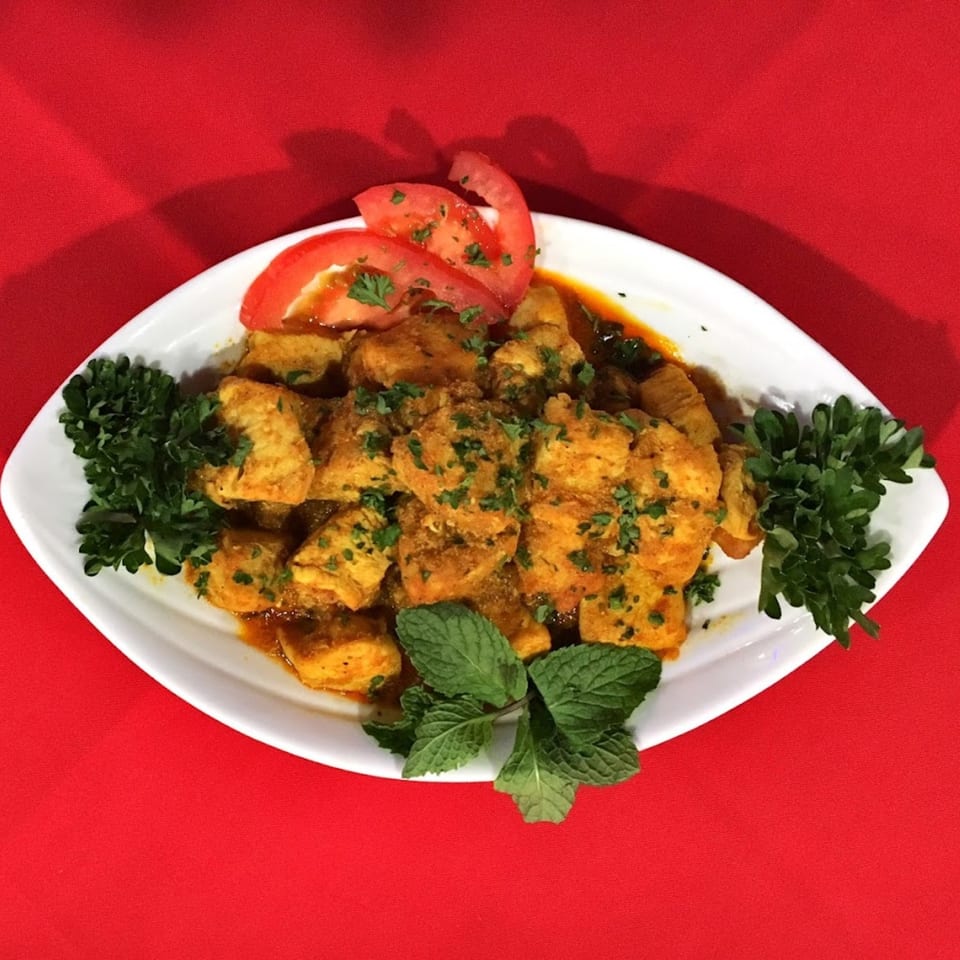 Indian chicken curry with fresh herbs and tomato slices on a white platter.