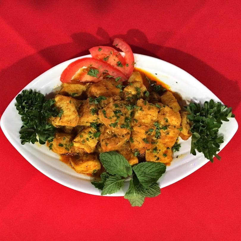 Indian chicken curry with fresh herbs and tomato slices on a white platter.