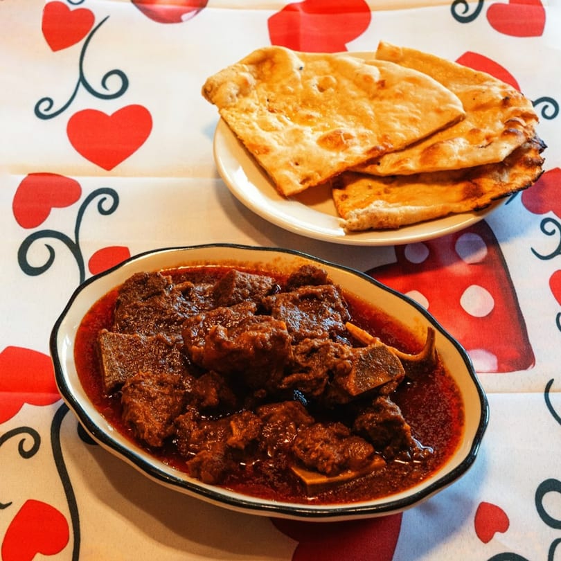 Indian lamb curry with naan bread on a white tablecloth with red heart patterns.