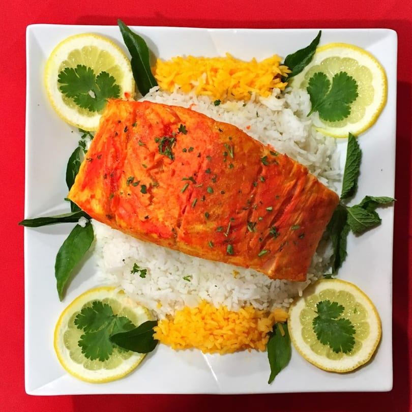 Indian salmon dish with white and yellow rice, garnished with lemon slices and herbs.