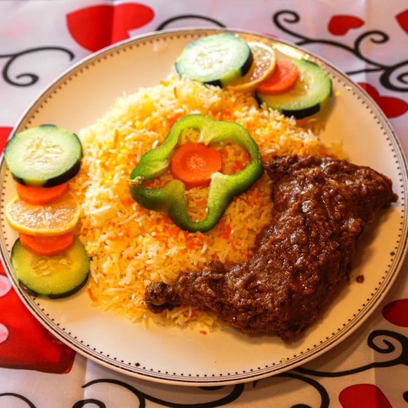 Indian chicken biryani with rice, cucumber, lemon, and carrot slices on a white plate.